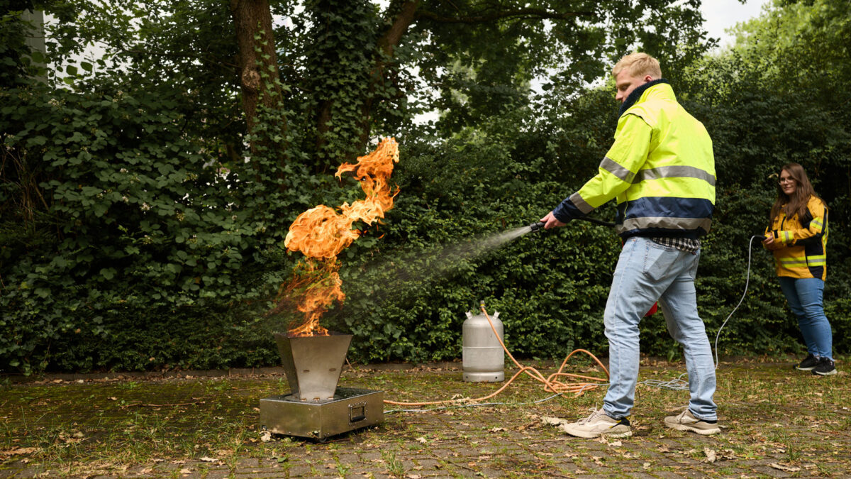 Ein Mann in Sicherheitsjacke löscht bei einer Brandschutzübung ein Feuer mit einem Feuerlöscher.