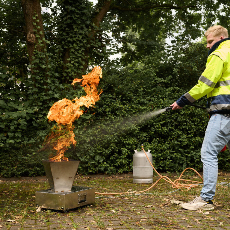 Ein Mann in Sicherheitsjacke löscht bei einer Brandschutzübung ein Feuer mit einem Feuerlöscher.