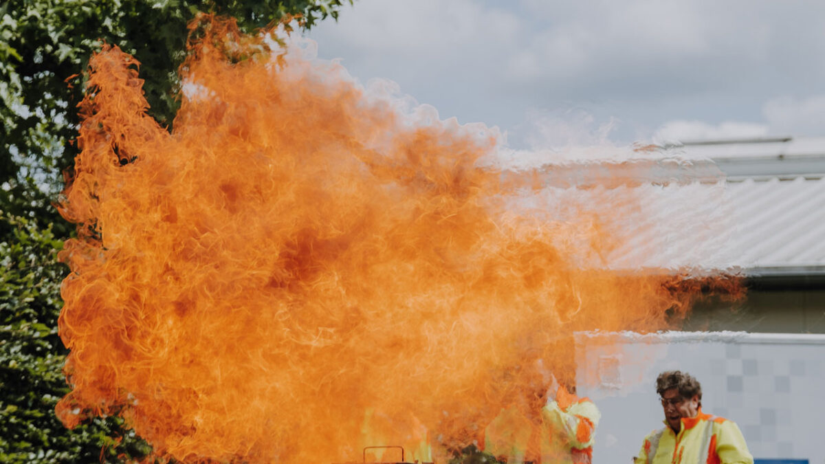 Brandschutzübung vor einem Unternehmen. Ein großes Feuer und zwei Menschen mit Feuerlöschern.