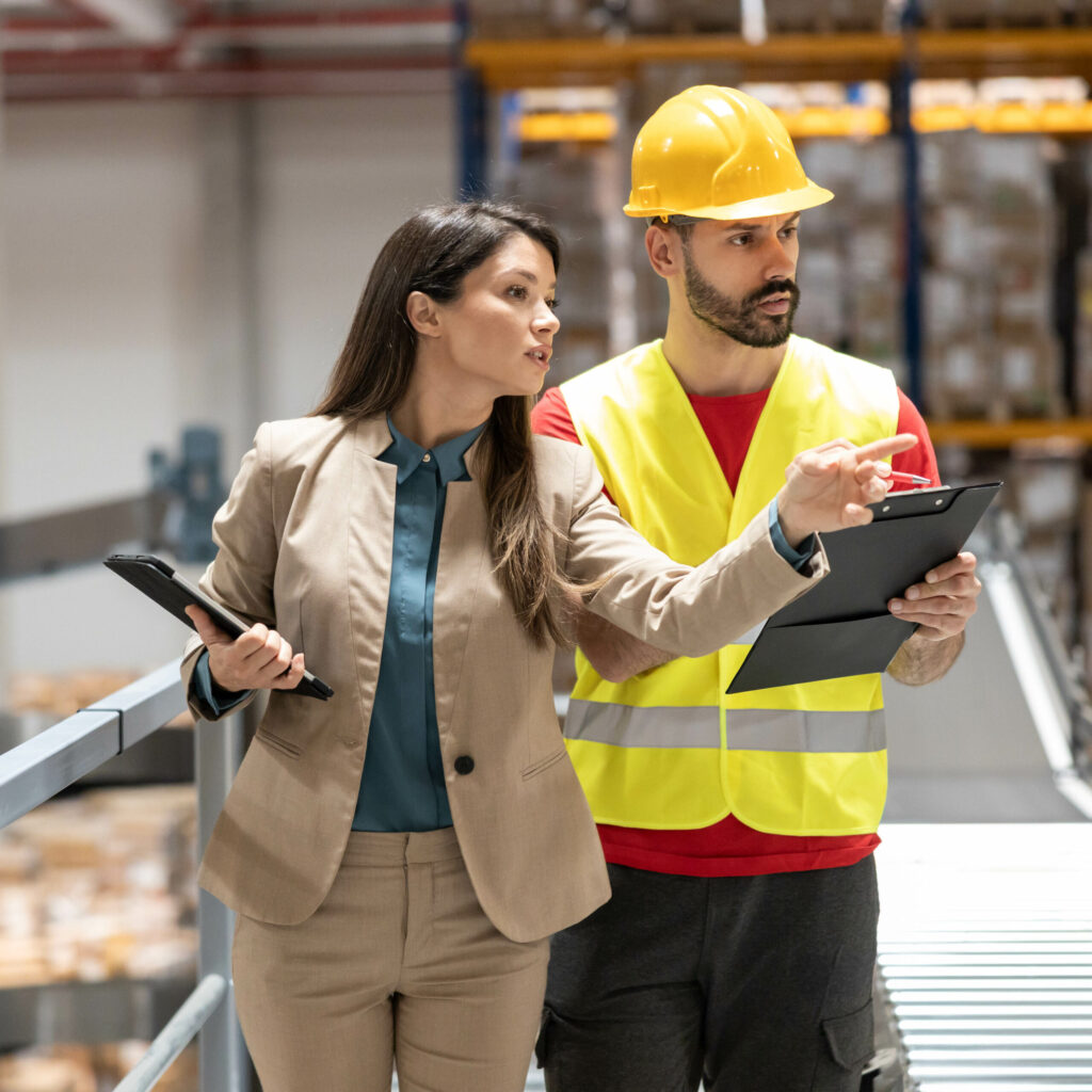 The manager explains safety procedures to a safety officer in the warehouse, emphasizing the importance of proper protocols.