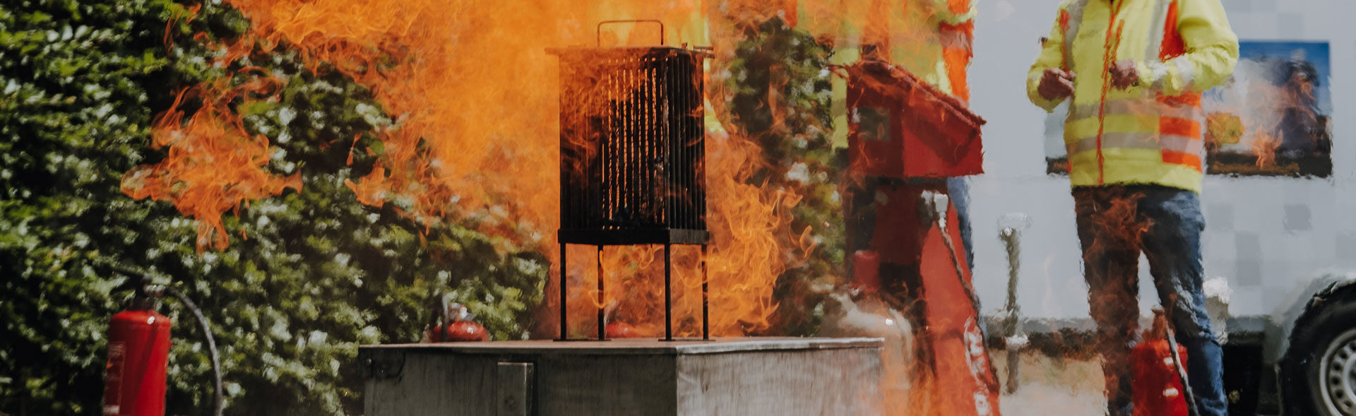Brandschutzübung vor einem Unternehmen. Ein großes Feuer und zwei Menschen mit Feuerlöschern.