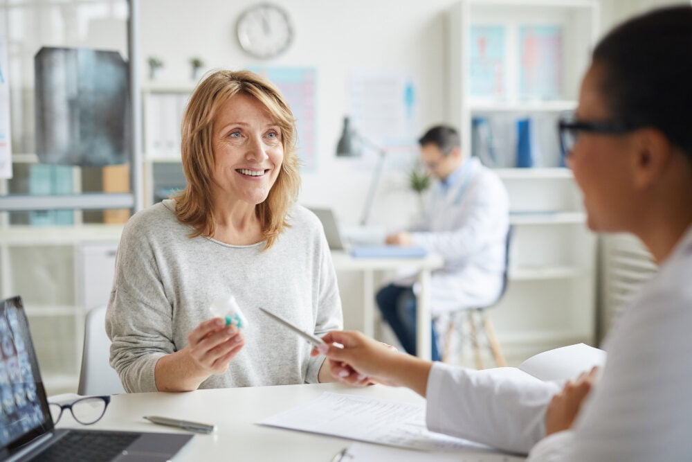 Eine Mitarbeiterin sitzt im Büro im Gespräch mit einer Betriebsärztin.