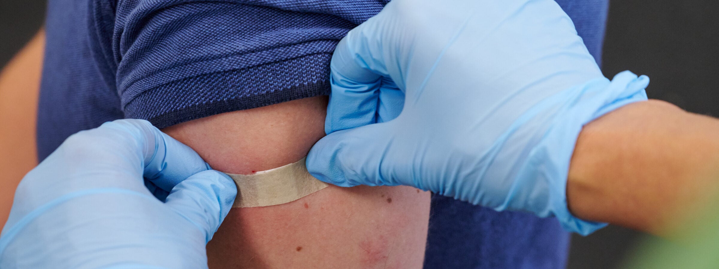 Eine Ärztin mit Handschuhen klebt einer Person nach dem Impfen ein Pflaster auf den Arm.