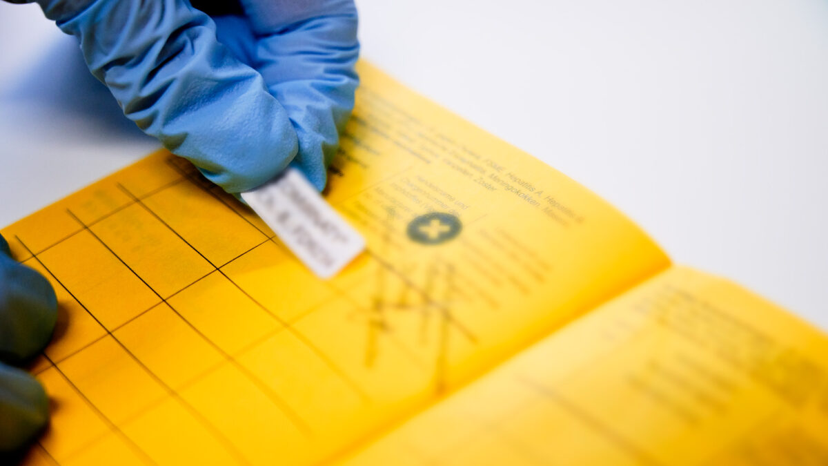 Eine Ärztin mit Handschuhen klebt einen Impfsticker in einen Impfpass.