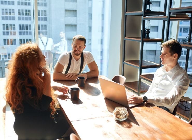 Lockeres Meeting von drei Mitarbeitenden im Pausenraum eines Unternehmen.