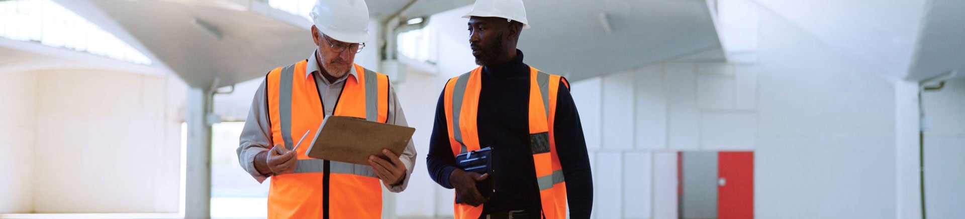 Fachkräfte für Arbeitssicherheit unterhalten sich in einer Lagerhalle über die Verkehrssicherheit im Unternehmen.