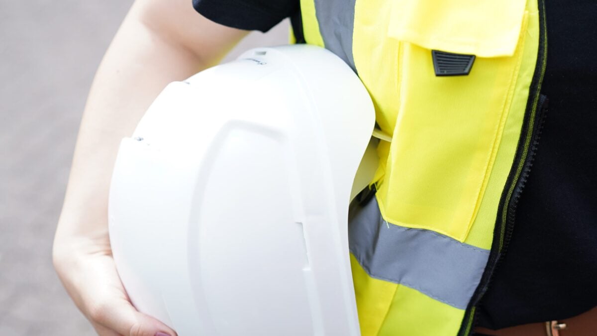 Eine Frau in Warnweste hält einen Schutzhelm unter dem Arm.