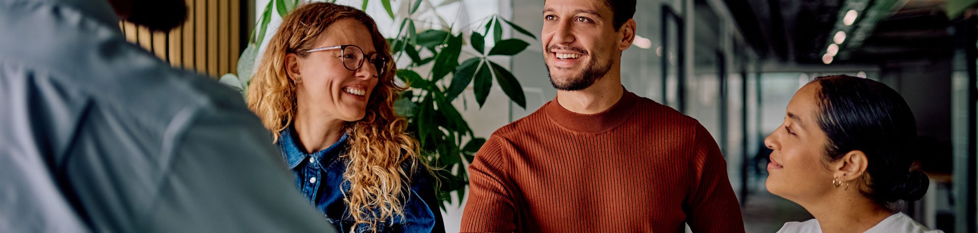 Vier glückliche Mitarbeitende lachen sich an und geben sich die Hand in einem Büro.