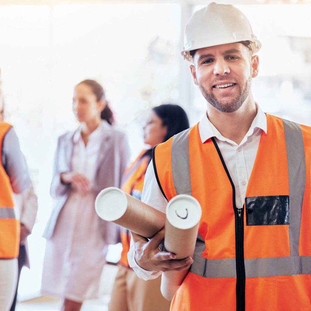 Eine Fachkraft für Arbeitssicherheit in einer orangenen Warnweste vor einer Gruppe Mitarbeitender.