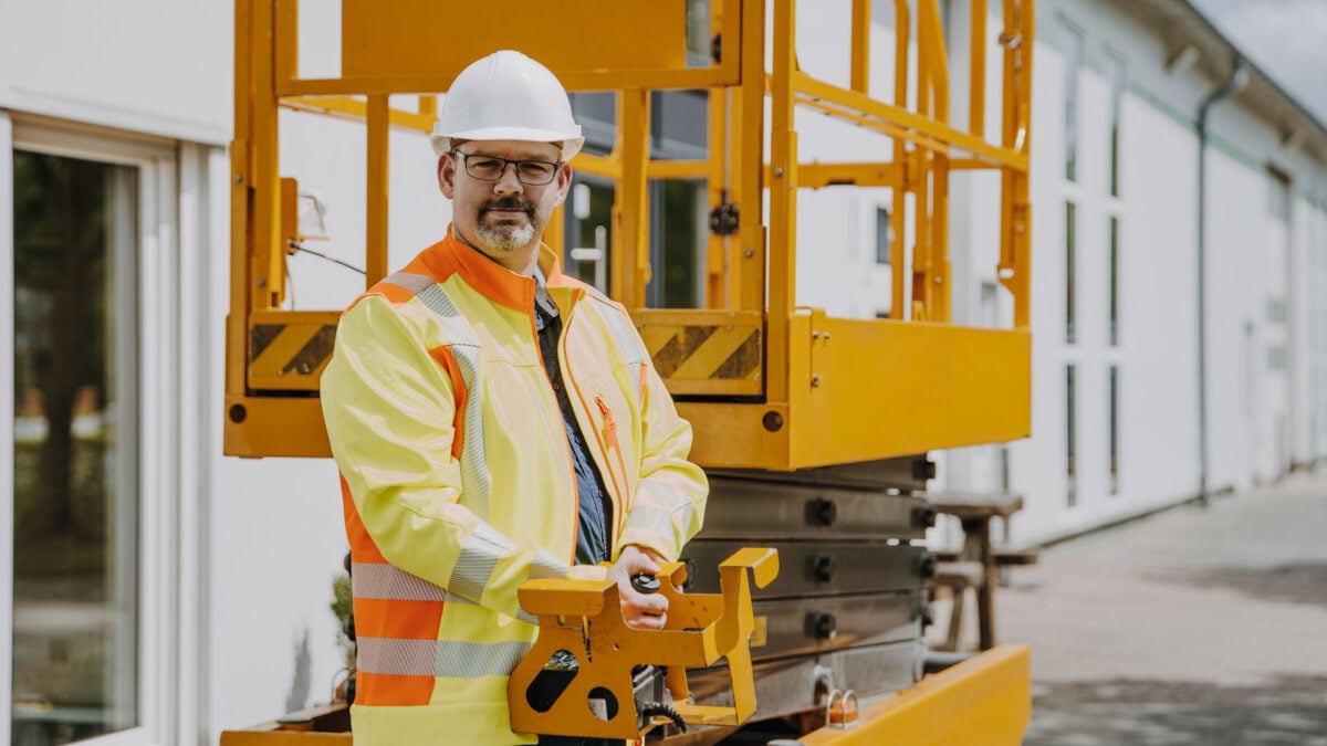 Ein SiGeKo in PSA vor einer Hebebühne auf einer Baustelle.