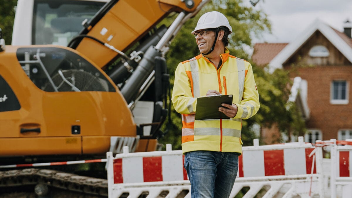 Ein Sicherheits- und Gesundheitskoordinator vor einem Bagger auf einer Baustelle.